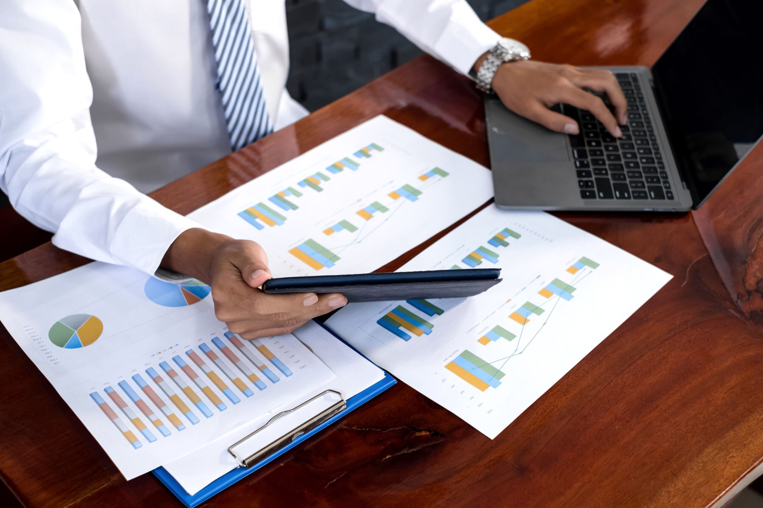 Person sitting at a desk comparing paper reports of various income streams.