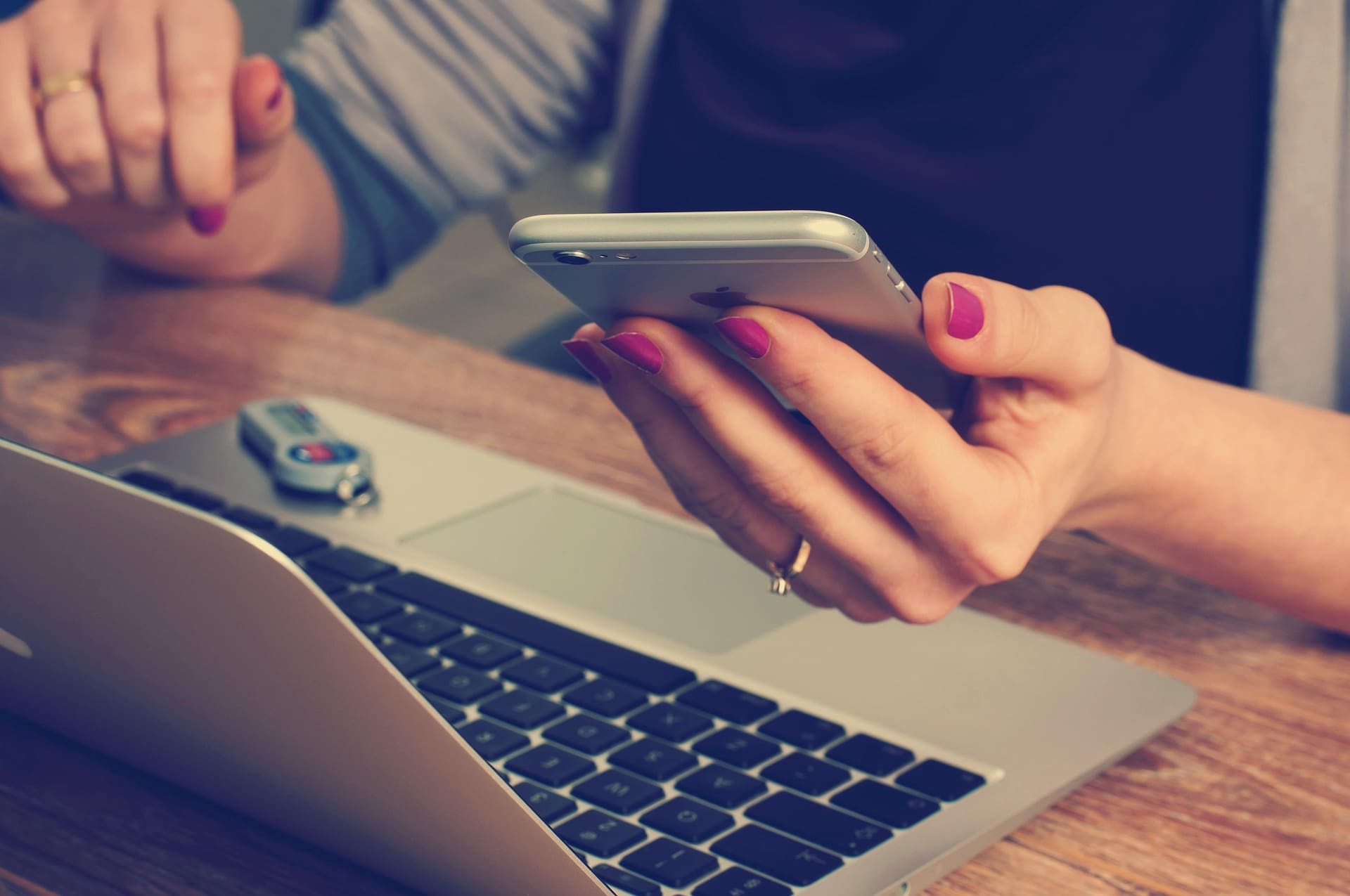 Business woman's hand holding a phone and sitting in front of a laptop computer